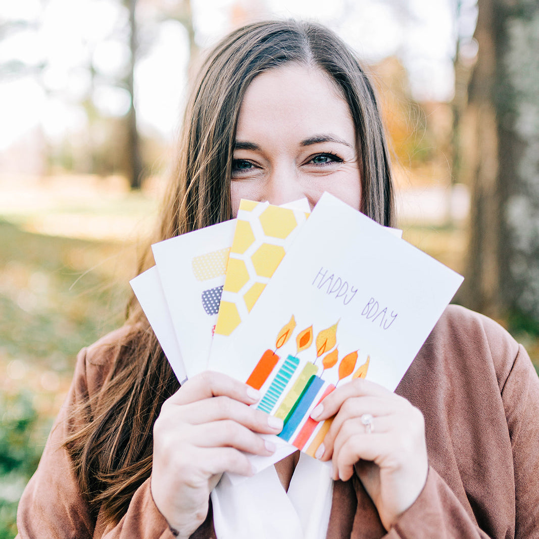Kayla Hutchinson, Founder and Owner of Lucky Dog Design Co., holding up greeting cards and smiling